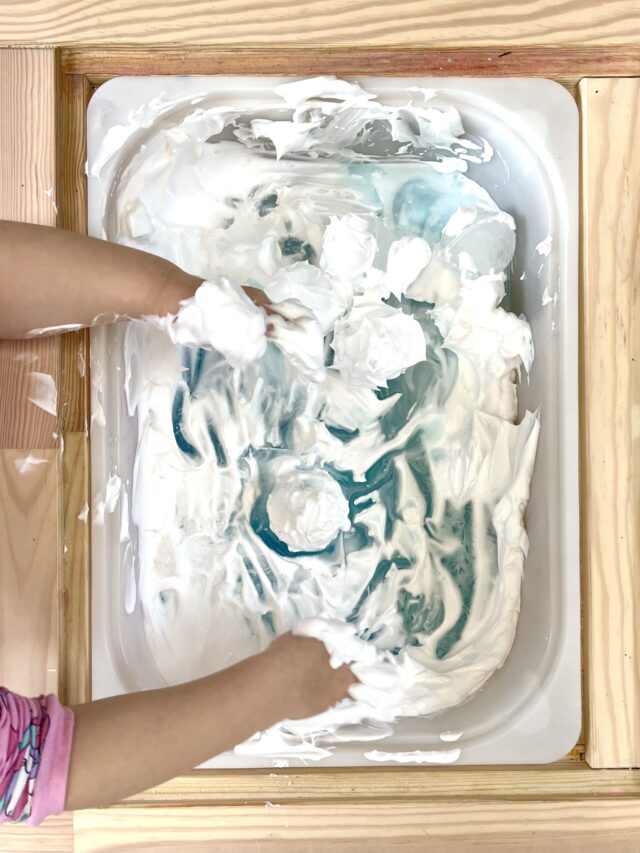 Tiny Messy Hands Playing With Ice Balls in Sensory Bin FIlled With Frozen Blue Water and Shaving Cream