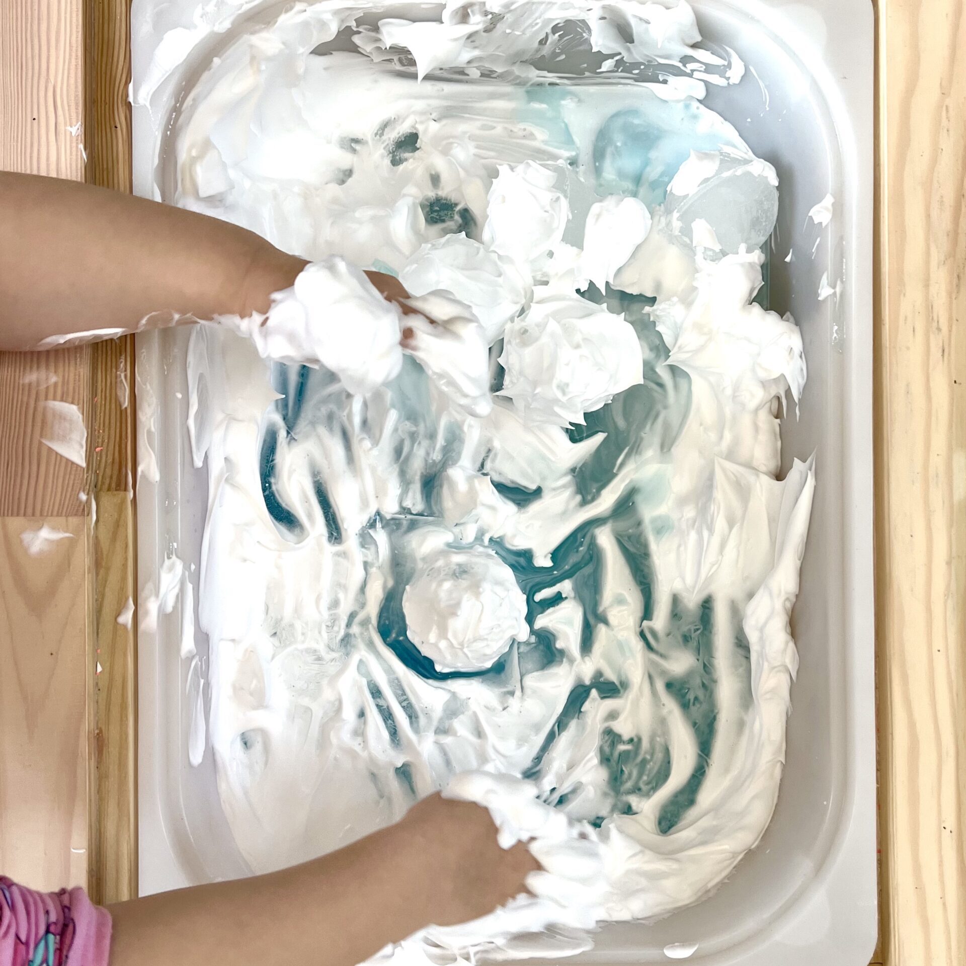 Tiny Messy Hands Playing With Ice Balls in Sensory Bin FIlled With Frozen Blue Water and Shaving Cream